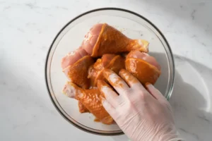 Hähnchenschenkel in einer Glasschüssel gleichmäßig mit Honig-Senf-Marinade bedeckt.