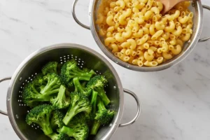 Vorbereitung für Brokkoli-Nudel-Auflauf: Gekochte Hörnchen-Nudeln und blanchierte Brokkoliröschen in Metallsieben auf einer Marmor-Arbeitsplatte.