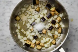 Zwiebeln und Auberginenwürfel werden in Olivenöl mit Salz angeschwitzt.
